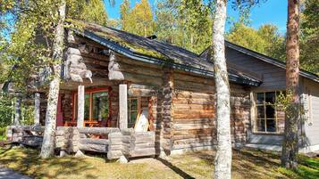 A log cabin with a porch, wooden deck, and a large window.