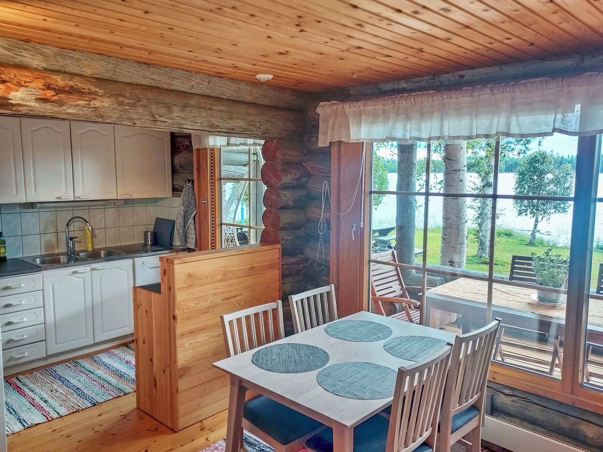 Ein Interieur einer Hütte mit Küche, Essbereich und großen Fenstern, die einen Ausblick ins Freie bieten.