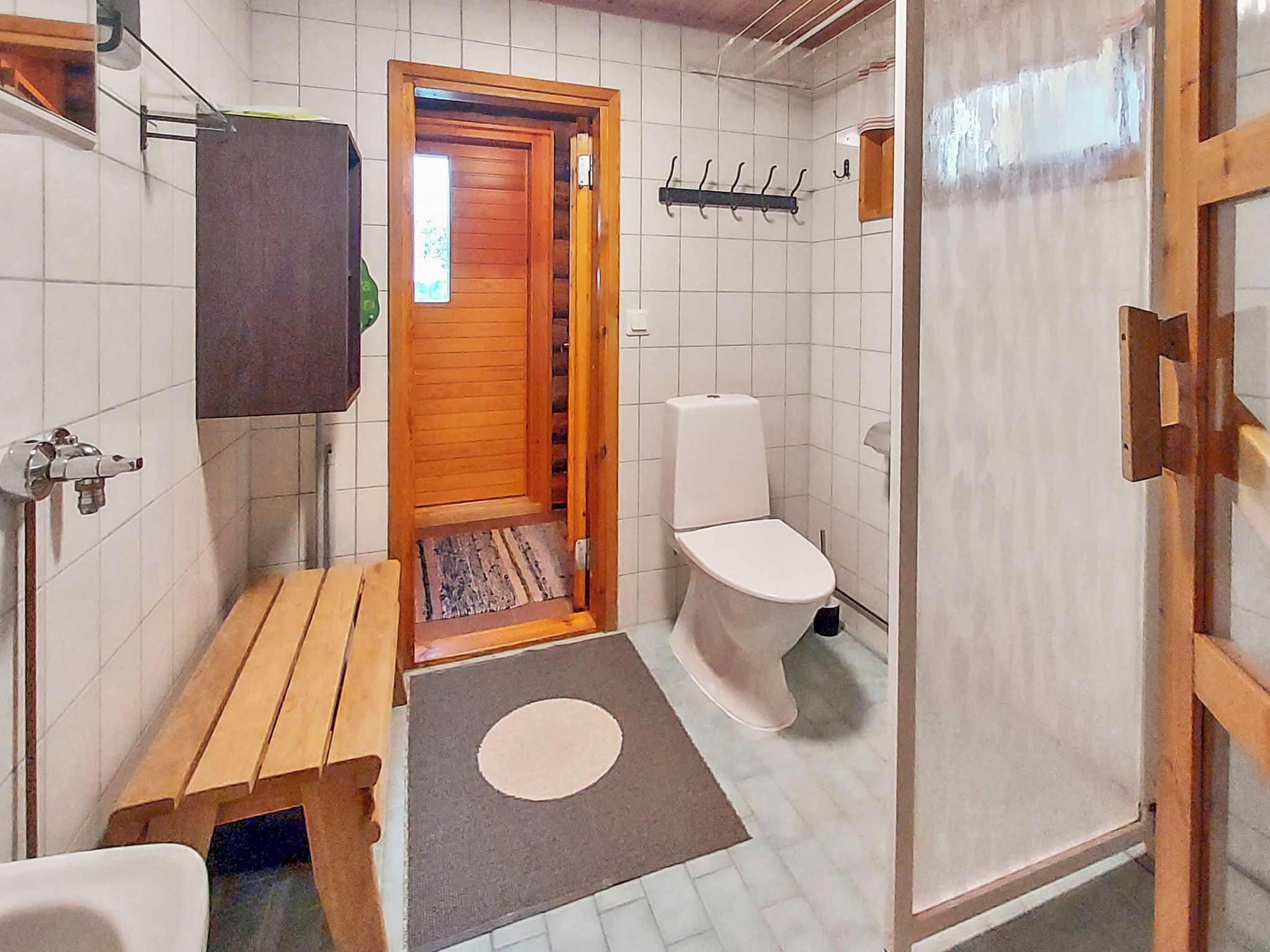 Un baño pequeño con un banco de madera, un inodoro y zona de ducha.