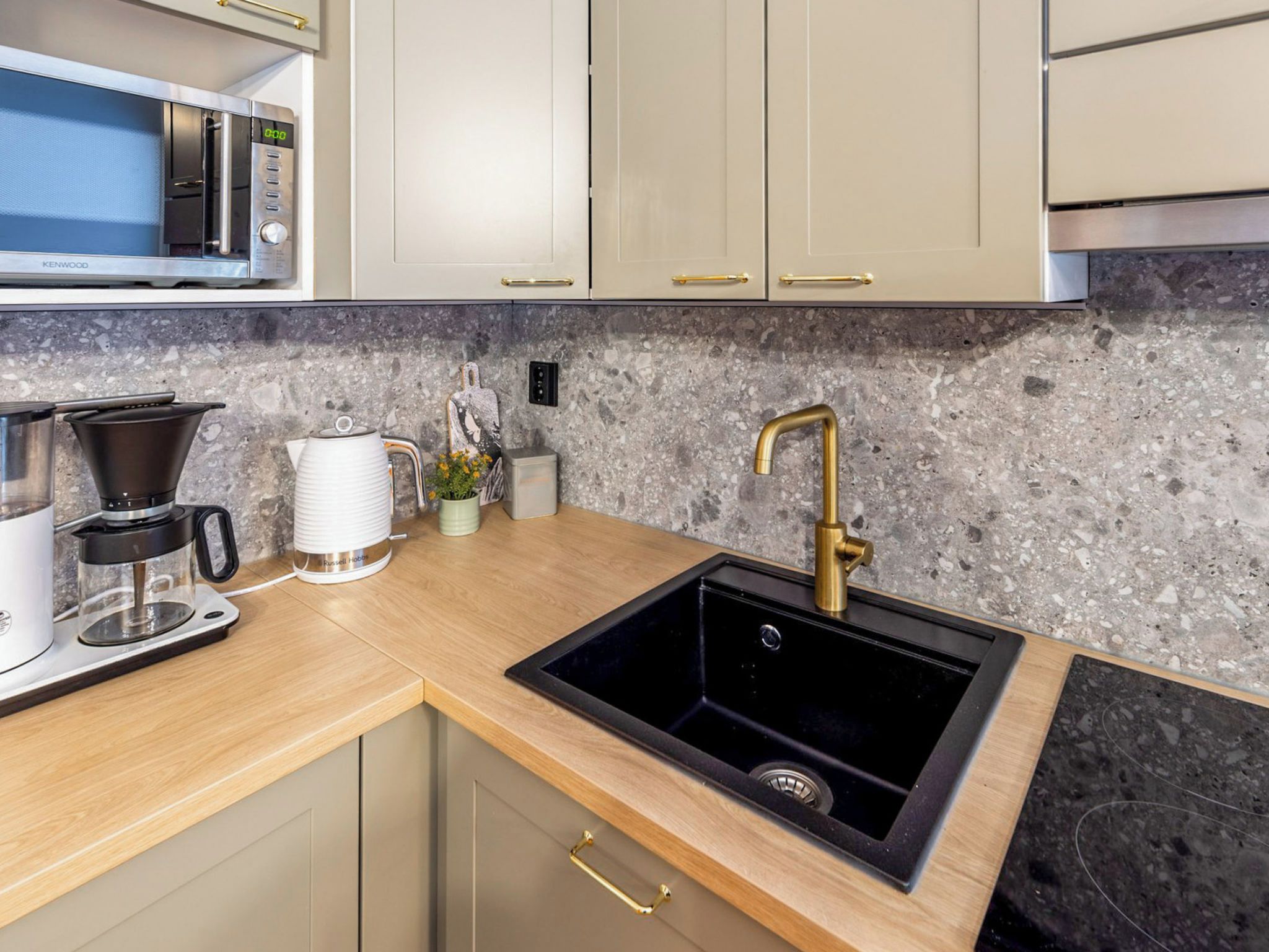 A modern kitchen with a granite countertop, stainless steel appliances, and a gold faucet.