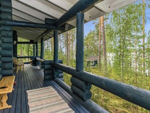 Une cabane en rondins avec une terrasse en bois, un banc et une vue sur une forêt.