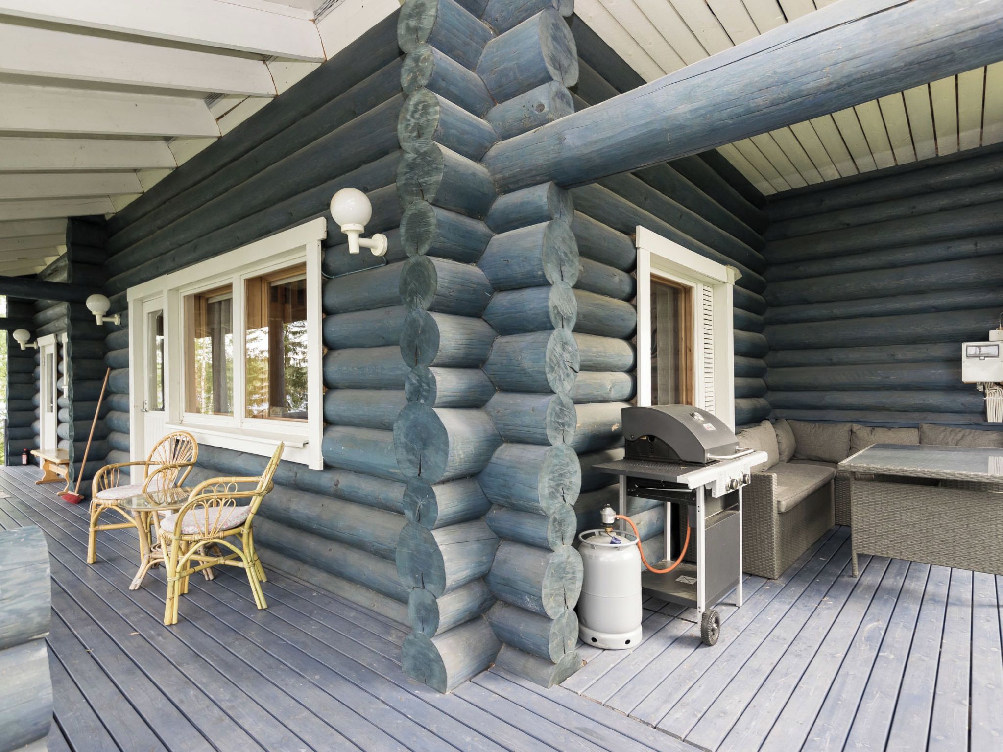 Eine Blockhütte mit Veranda, Grill, Korbmöbeln und einem Gasflaschen.