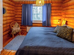 Une chambre dans un chalet en rondins, avec un lit, une chaise, une fenêtre avec des rideaux et un luminaire suspendu.