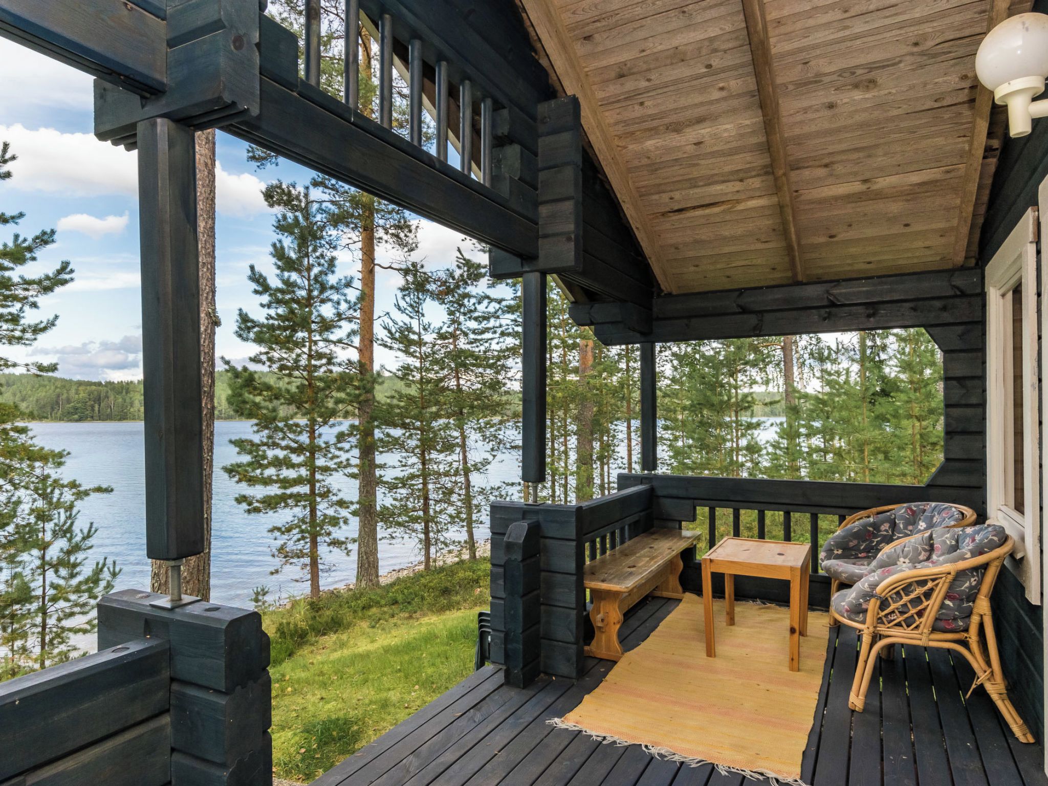 A wooden deck with a bench and table, overlooking a lake with trees.