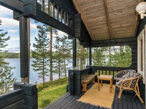 A wooden deck with a bench and table, overlooking a lake with trees. - Joutsen by Interhome (Puumala)