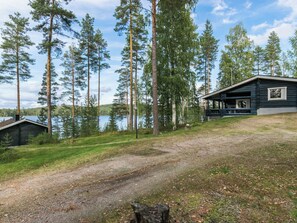 Une cabane dotée d’une véranda, entourée de grands arbres et bordée par un lac.