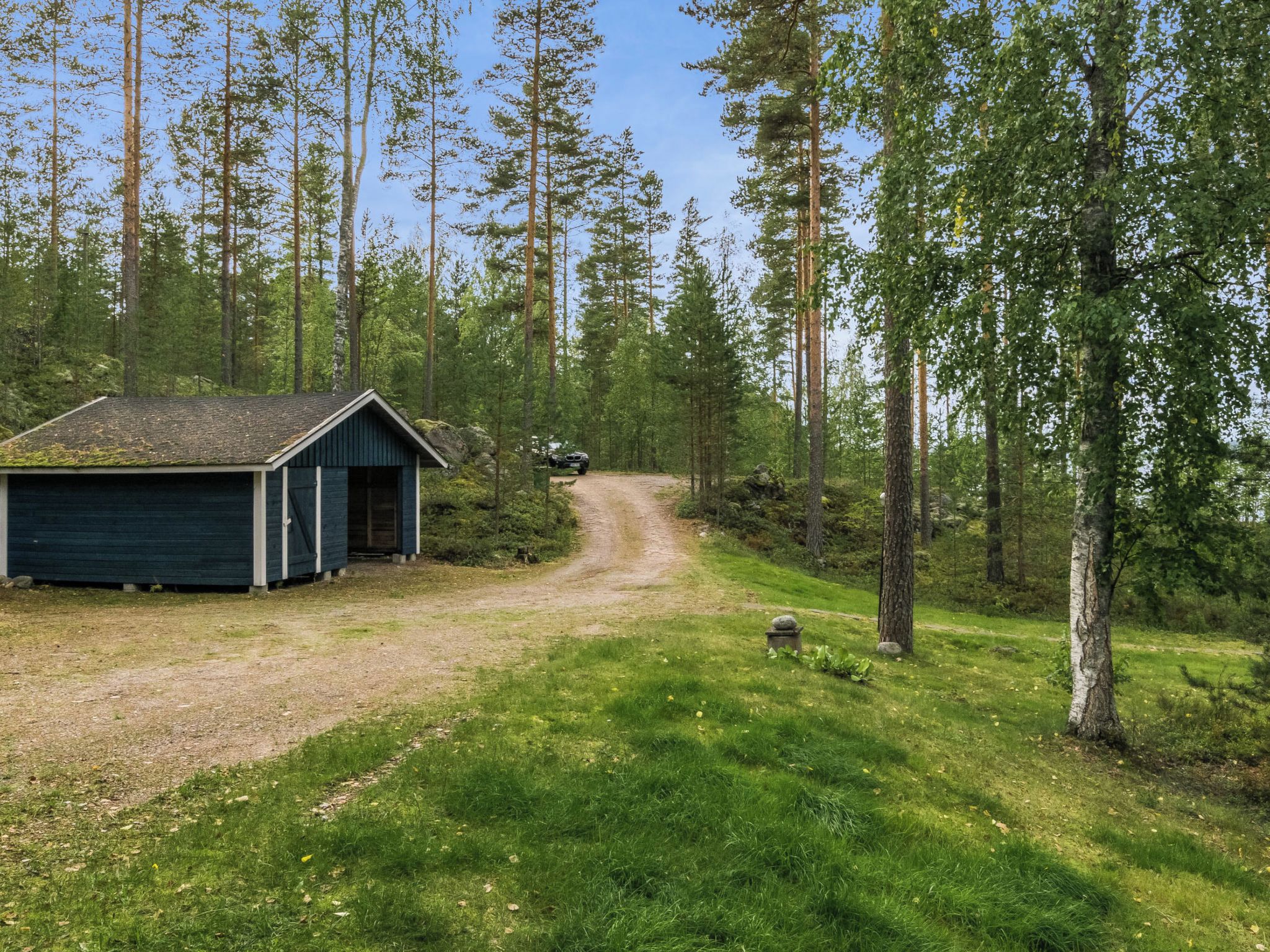 Mökki, jonka luo johtaa sorainen polku, ja jonka ympärillä on metsä.