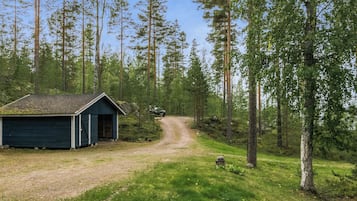 Mökki, jonka luo johtaa sorainen polku, ja jonka ympärillä on metsä.