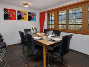 A dining area with a wooden table, black chairs, and a view of mountains through large windows.