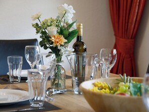 Une table à manger dressée avec de la belle verrerie transparente, une bouteille de vin et un centre de table floral.