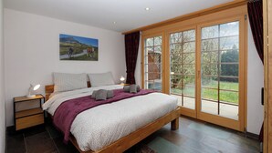 Un dormitorio con una cama grande, una mesita de noche, una lámpara de noche, una ventana con cortinas y un cuadro en la pared.