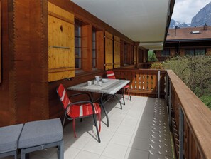 Un balcon en bois avec une table et des chaises, une vue sur les montagnes et un bâtiment avec un toit en tuiles.