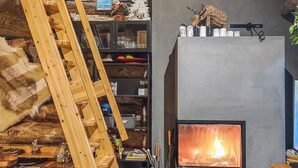 Tunnelmallinen huone, jossa on takka, puinen tikapuu, hyllyjä erilaisine esineineen ja kiviseinä.