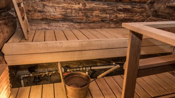 Sauna, jossa on puiset lauteet ja metallinen ämpäri.