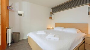 Een hotelkamer met een groot bed, een houten hoofdbord, een nachtkastje met een lamp, een kleine prullenbak en een radiator.