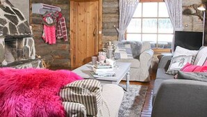 A cozy log cabin interior with a stone fireplace, a sofa, and a dining table.