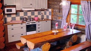A rustic cabin kitchen with a wooden table, a stove, and a window with curtains.