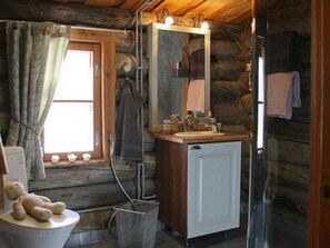 A rustic cabin bathroom with a wooden interior, a sink with a mirror above it, and a window with curtains. - Kopinkallio 2 by Interhome (Asikkala)