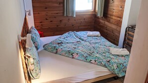 A wooden-paneled room with a bed, a window with curtains, and a wall-mounted lamp. - Apartment Girun by Interhome (Flims)