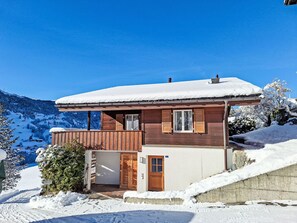 A wooden chalet with a snow-covered roof, a wooden balcony, and a small garage. - Ahornen by Interhome (Grindelwald)
