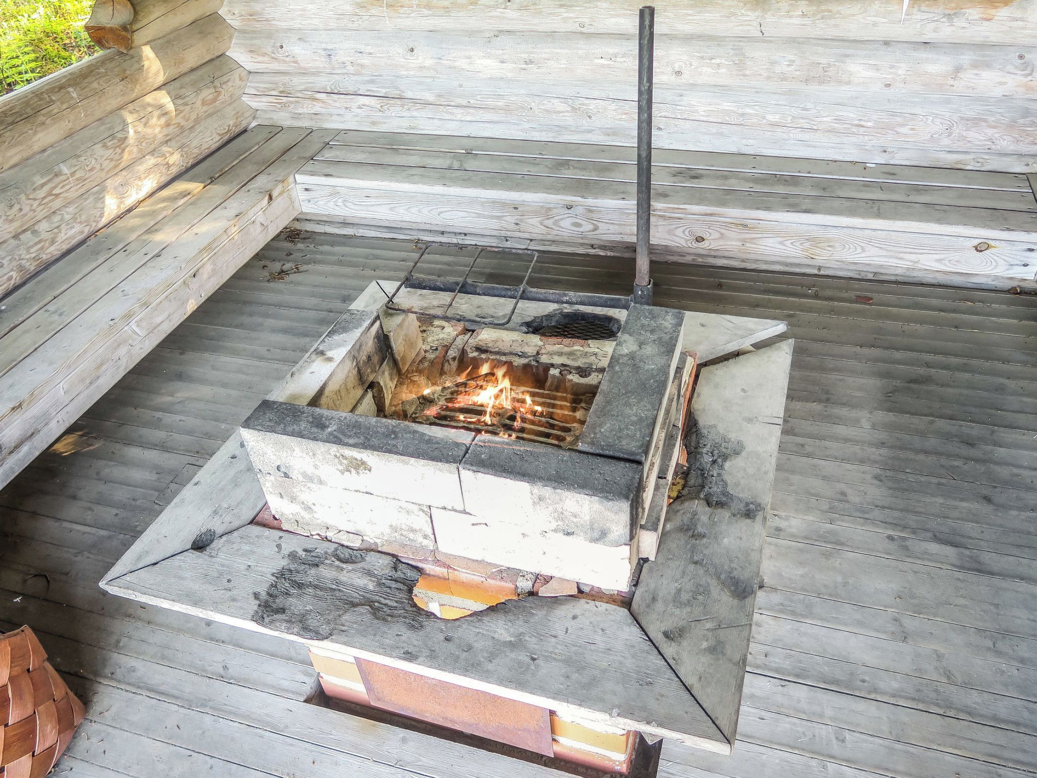 A square outdoor fire pit with a chimney, surrounded by a wooden deck.