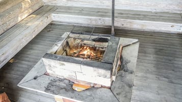 A square outdoor fire pit with a chimney, surrounded by a wooden deck.