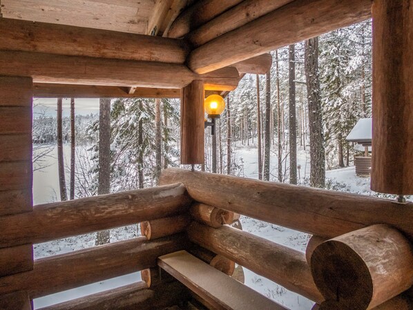 A log cabin interior with a bench and a window overlooking a snowy forest.