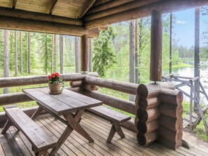 Una terraza de madera con una mesa de picnic y bancos, con vistas a un área boscosa y una masa de agua.
