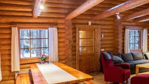 Ein Blockhaushaus-Interieur mit einem Holzespeisesaal, Bänken, einer Couch und einem Kamin.