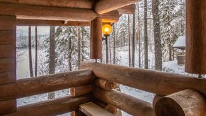 Ein Holzblockhaus-Interieur mit einer Bank und einem Fenster mit Blick auf einen verschneiten Wald.