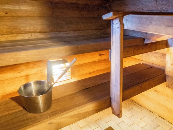 Sisustus on tehty puusta, ja siellä on metallinen ämpäri sekä puinen penkki.