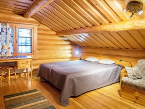 A wooden cabin interior with a bed, desk, and chair.