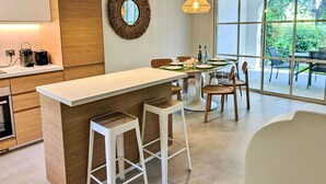 A modern kitchen with a central island, bar stools, and a dining area with a view of the outdoors. - Les Restanques Golfe Saint Tropez by Interhome (Grimaud)