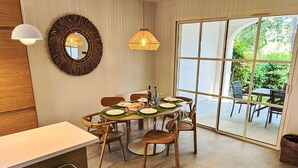 A dining area with a round table set for four, surrounded by wicker chairs. A large window provides a view of the outdoors. - Les Restanques Golfe Saint Tropez by Interhome (Grimaud)
