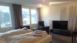 Una camera d'albergo con un letto grande, una televisione a schermo piatto e vista su un paesaggio innevato dalle finestre.