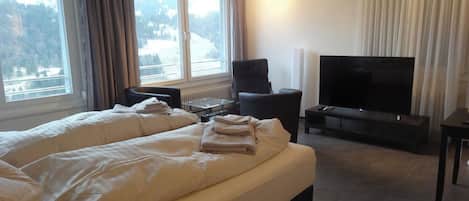 Habitació d'hotel amb un llit gran, un televisor de pantalla plana i vista a un paisatge nevós per les finestres.