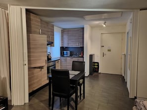 A compact kitchen with modern appliances, a dining area with a table and chairs, and a door leading to another room. - Barbara West Appartement/Fewo 2-Bettwohnung by Interhome (Engelberg)