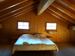 Ein Zimmer mit Holzwänden, einem Bett, zwei Fenstern und einem Nachttisch mit Lampe.