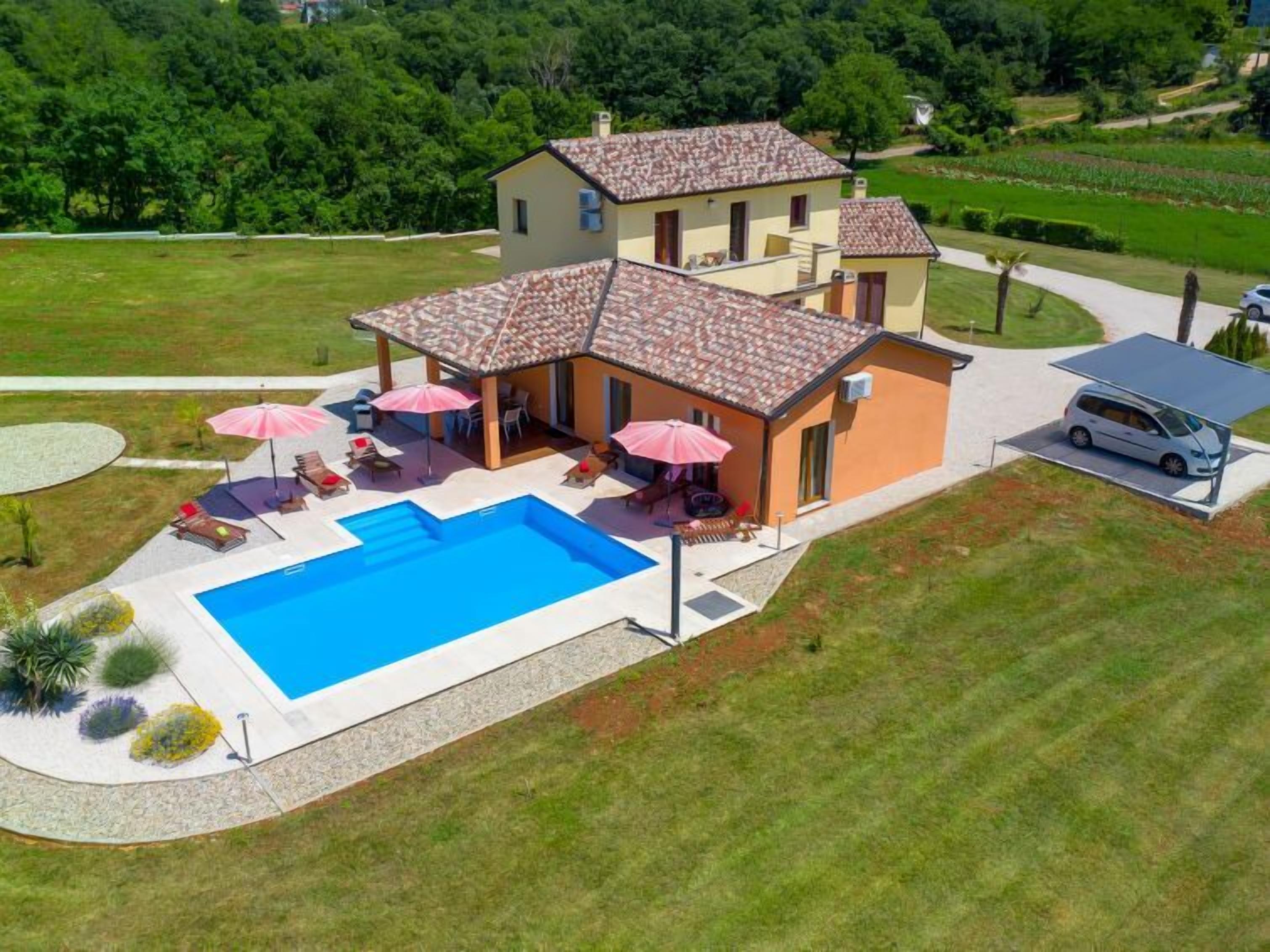 Una casa de dos pisos con piscina, mobiliario exterior y un coche aparcado.