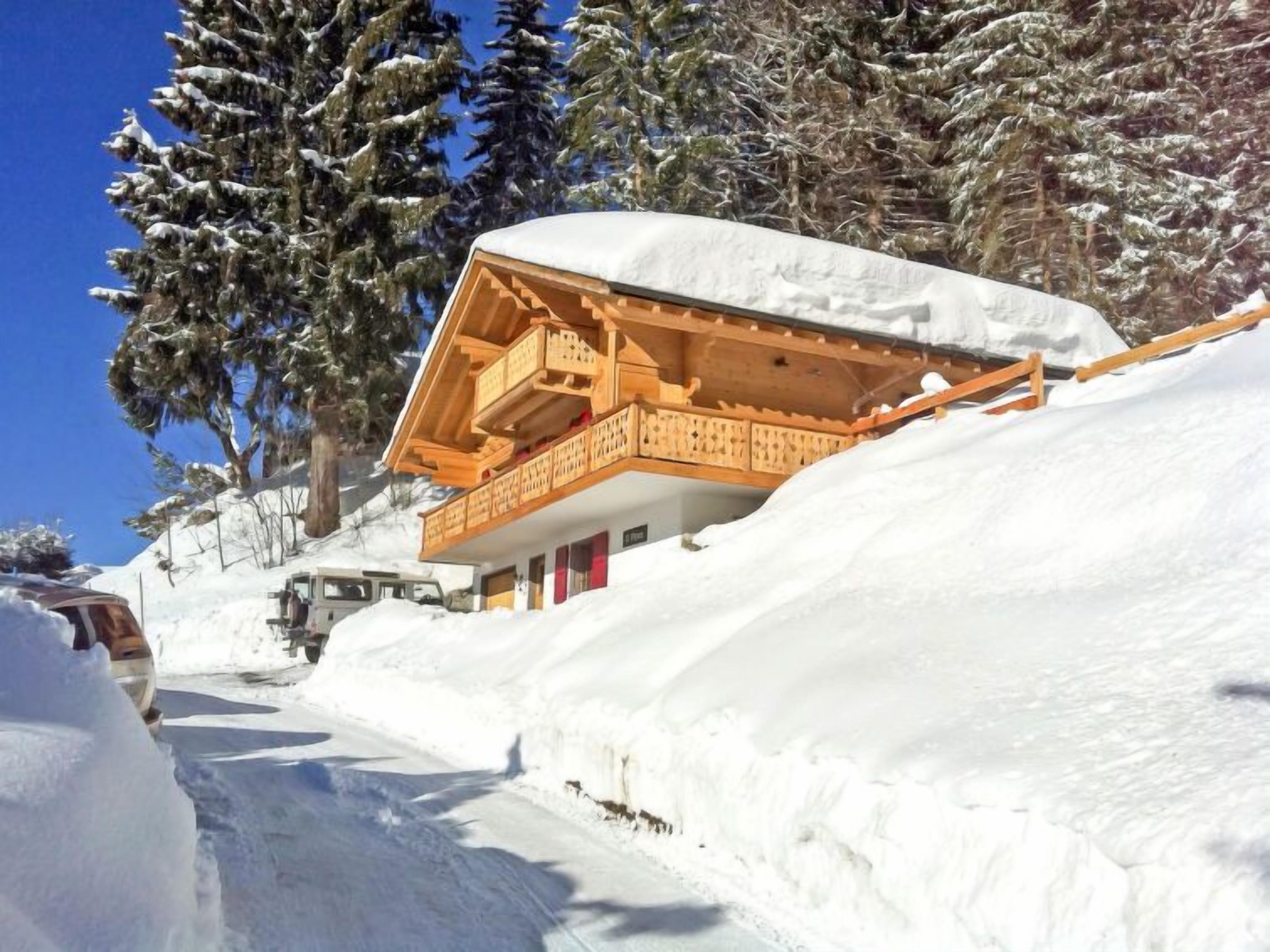 Una cabaña de madera con balcón, rodeada de árboles cubiertos de nieve y un cielo despejado.