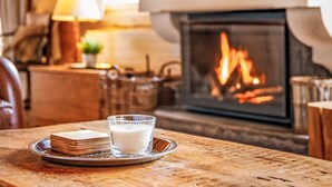 A cozy room with a fireplace, a table with a glass of milk and a stack of books, and a lamp on a side table. - Saint Piran by Interhome (Villars)