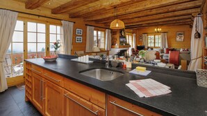 A kitchen with wooden cabinets, a black countertop, a sink, and a dining area with a sofa and table. - Saint Piran by Interhome (Villars)