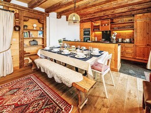 A wooden interior with a dining table set for four, a bench, and a kitchen area with wooden cabinets and appliances. - Saint Piran by Interhome (Villars)