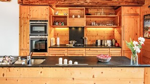 A wooden kitchen with built-in appliances, a central island, and a hanging light fixture. - Saint Piran by Interhome (Villars)