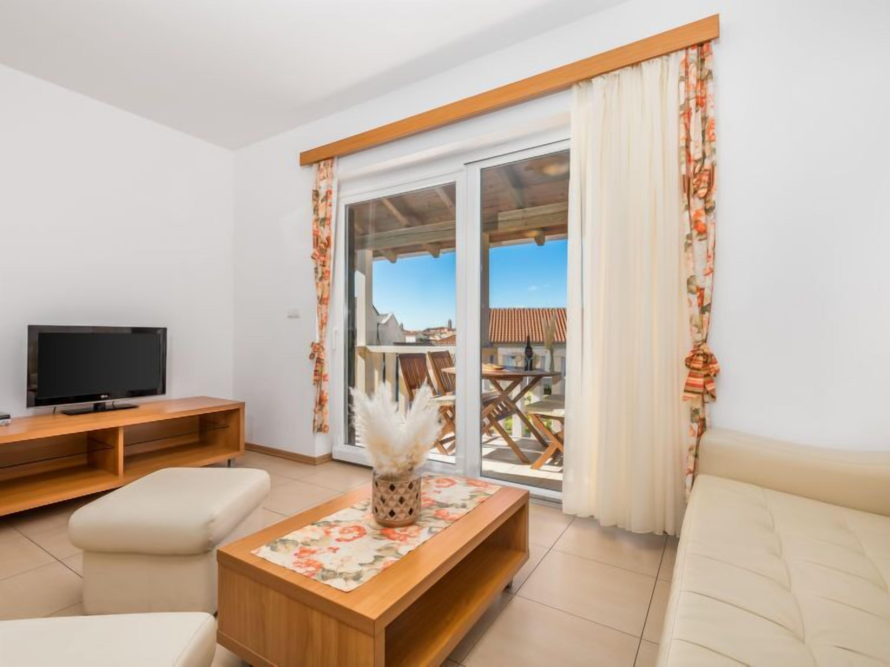 Una sala de estar moderna con una televisión de pantalla plana, muebles de madera y un amplio ventanal corredera que da a un área exterior.