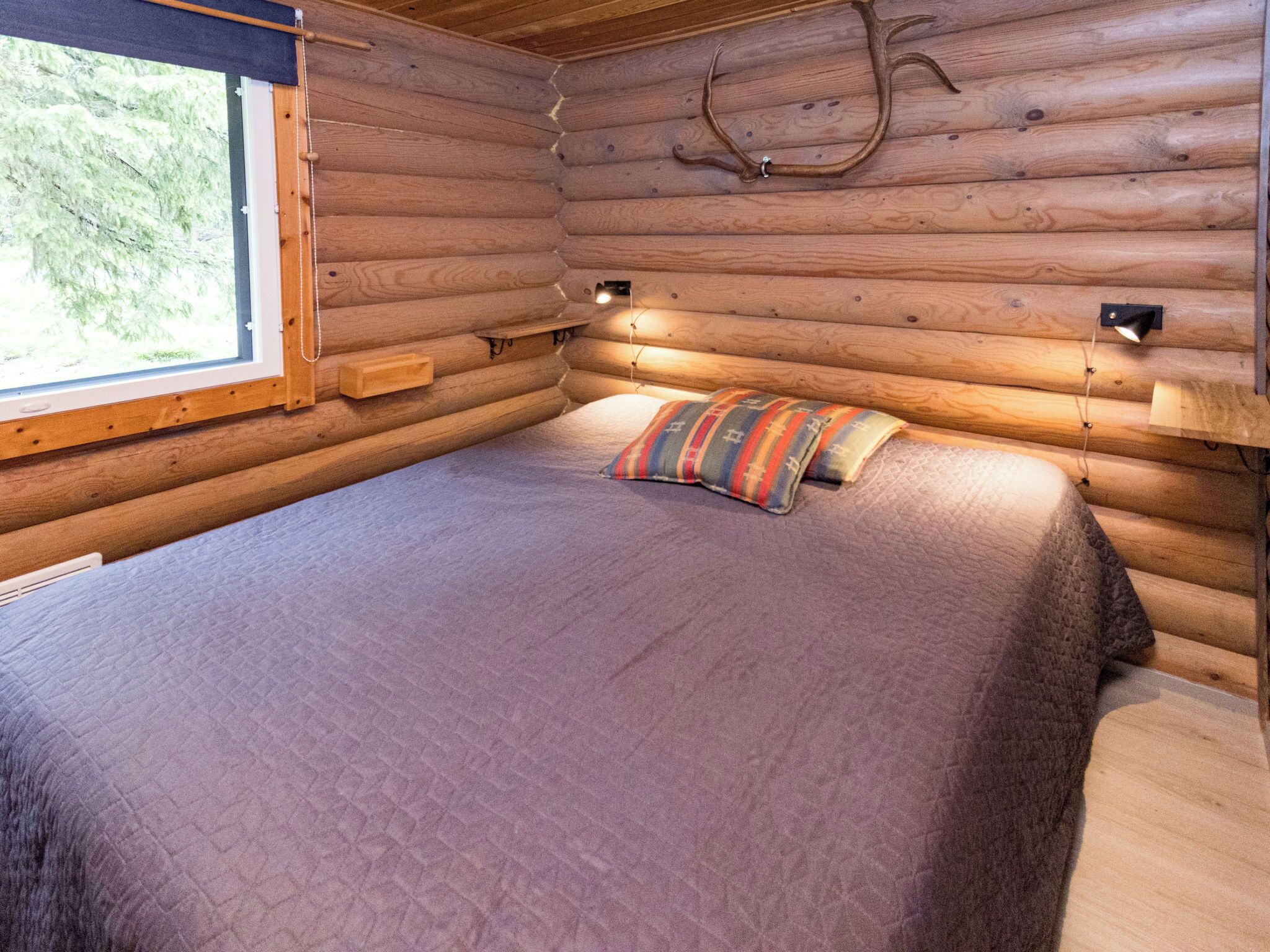 A log cabin room with a bed, a window, and a mounted deer antler.