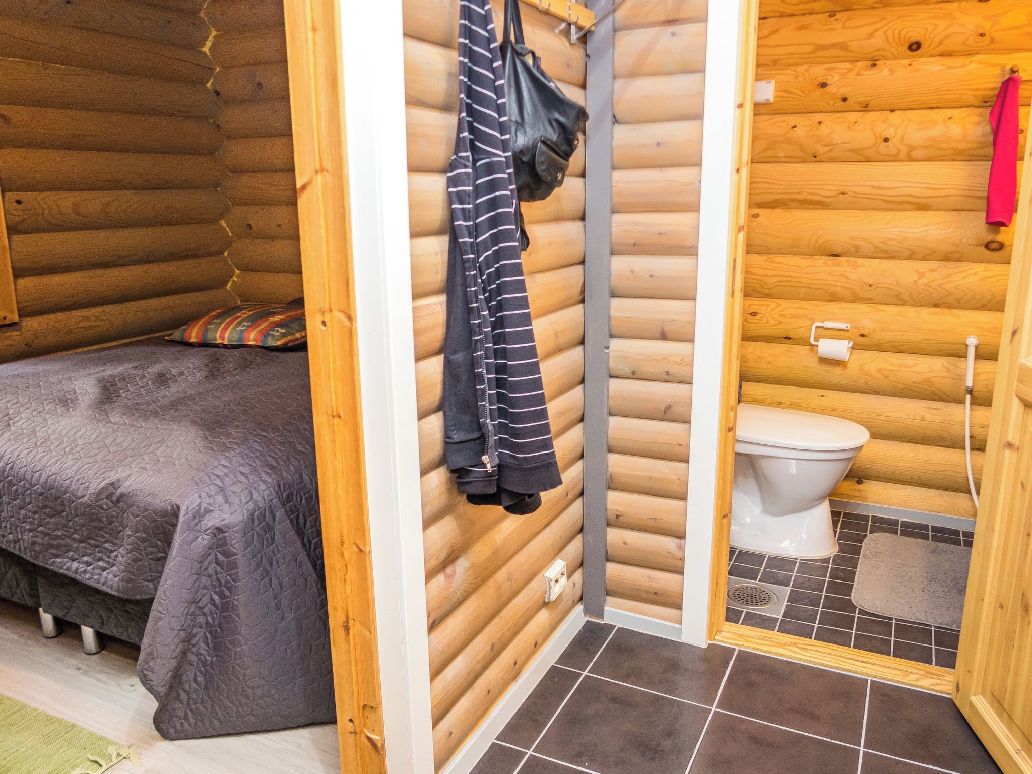 Una camera in una baita di legno con un letto, una borsa appesa e un gabinetto.