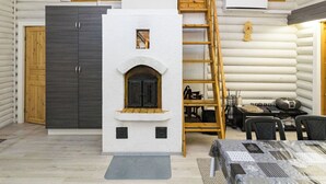 A log cabin interior with a central fireplace, wooden staircase, and a dining area with tables and chairs.