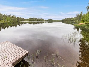 A calm lake with a wooden dock extending into the water, surrounded by dense forest.
