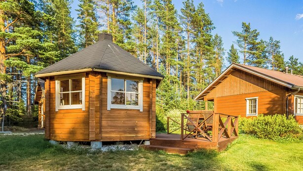 Une cabane en bois avec un petit porche et un bâtiment séparé doté d’un toit rouge.
